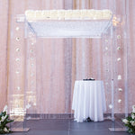A wedding chuppah decorated with bunches of white flowers along the top, carnations floating down the sides, and white flower decorations on the floor on either side.